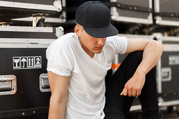 Fashion young man in a fashionable black cap with a stylish white t-shirt sitting near the boxes