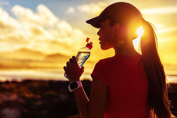 Fitness woman drinking water from sports bottle on afternoon workout after run training jogging outdoors at sunset.