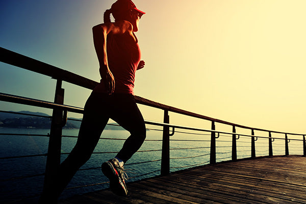 Young fitness woman running on sunrise seaside boardwalk